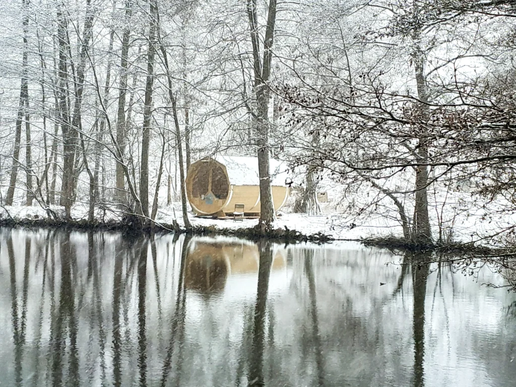 A small lake with a wooden sauna in a snow-covered winter landscape.